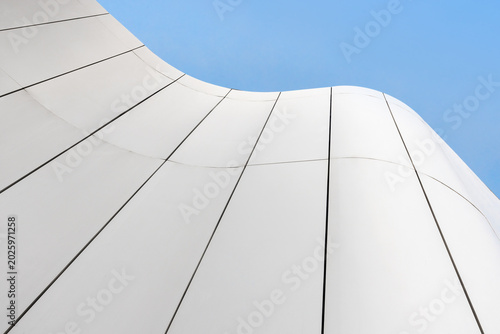 Abstract view of a modern white building facade with smooth curved panels and strong vertical lines, evoking minimalism, calm and contemporary architectural design against a clear blue sky