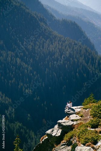 Obraz na płótnie Young woman sitting on cliff edge above deep forest valley in Fagaras Mountains, Romania