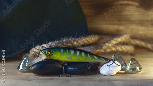 Foto Realistic fishing lure with treble hooks on wooden surface with stones and rope