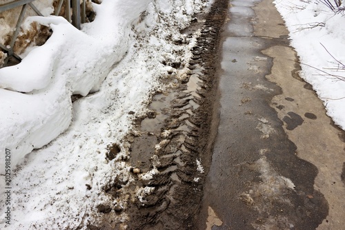 Photos Muddy tractor tracks deeply imprinted in slush alongside melting, grubby snow piles near a roadside fence