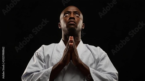 Black man in white karate gi with hands clasped in prayer pose looking upwards male
