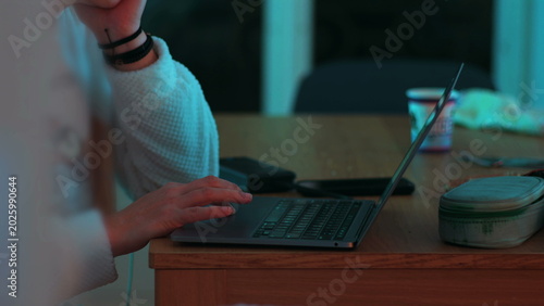 Close view of woman browsing on laptop at wooden table at night, online navigation session in calm domestic environment