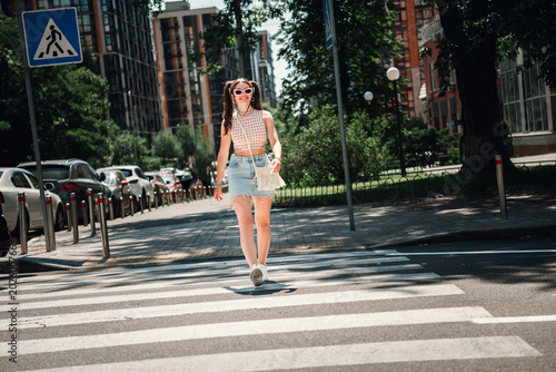 Foto Young woman crossing a sunny city crosswalk in a casual summer outfit smiling as