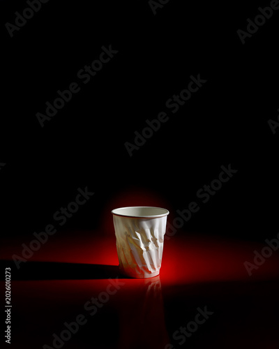 Crumpled white paper cup illuminated by dramatic red lighting against black . Mysterious studio composition creates moody, artistic atmosphere. For conceptual design and creative projects.
