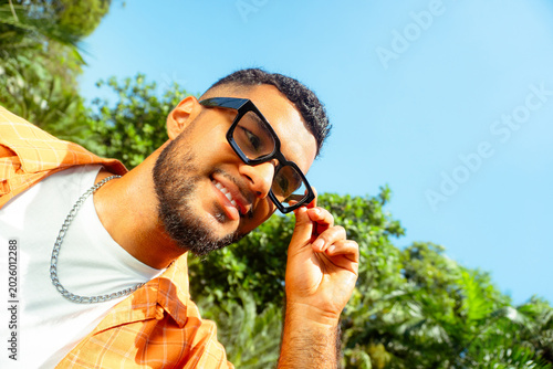 Young smiling man adjusting dark frame eyeglasses outdoors