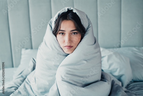 Bild auf Leinwand Tired woman wrapped in a blanket on bed looking unwell and seeking comfort after