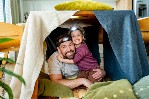 фотографія Dad and child building and playing in cozy blanket fort.