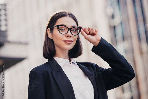 Foto Confident businesswoman in cat-eye glasses adjusts her frame outside a modern co