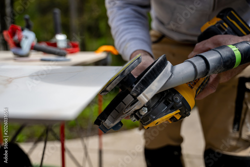 Fotografie Worker is polishing corner a ceramic tile with an electric grinder on a workbench during a home project
