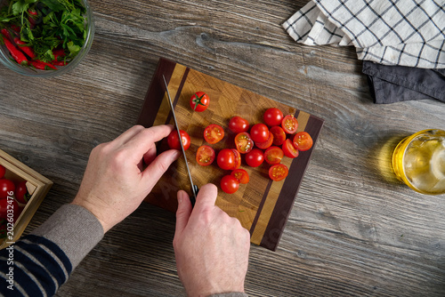 Foto A top view of a man cutting cherry tomatoes on a beautiful wooden board