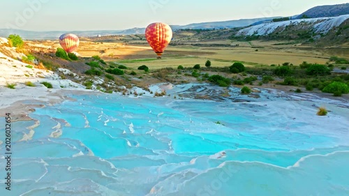 Drone view of Travertines of Pamukkale, Turkey. Hot air balloon floats above natural thermal pools and white limestone terraces at sunrise.