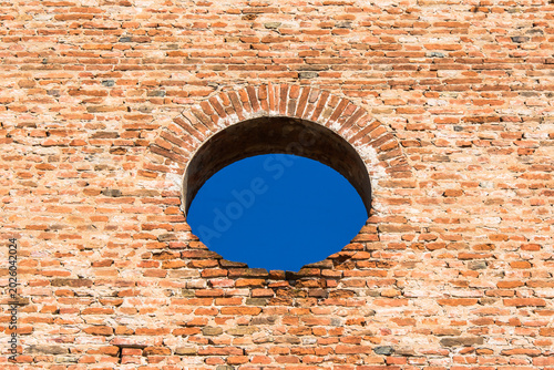 Dettaglio di un muro di mattoni con un  foro circolare ial centro da cui si vede il cielo