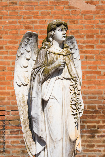 La statua di un angelo davanti a un muro di mattoni nel cimitero monumentale di Ferrara
