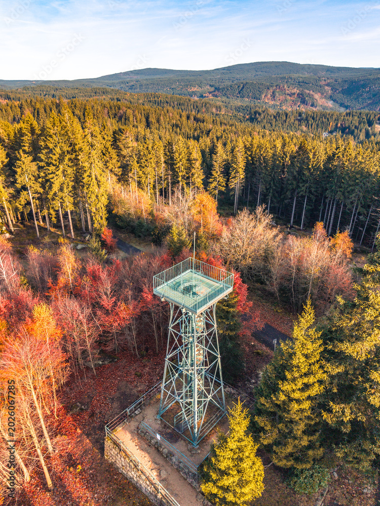 Fototapeta premium Slovanka Lookout Tower stands tall in the Jizera Mountains, showcasing vibrant autumn colors. This historic iron tower offers stunning views of the surrounding forested landscape.