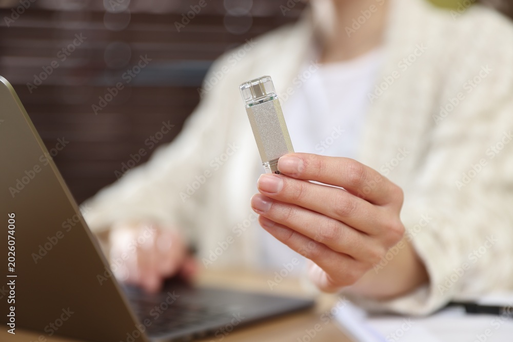 Fototapeta premium Woman with USB flash drive working on laptop at desk, closeup