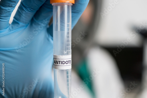 Quadro su tela Close up view of researcher or laboratory worker hand in blue glove holding a plastic tube with transparent liquid and antidote label on it