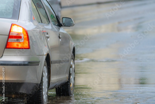 Car driving through flooded street during heavy rainfall with reflective wet road surface