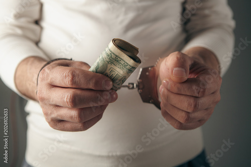 A man's hand holding a criminal's handcuffs, the concept of legality, and holding a dollar as a bribe