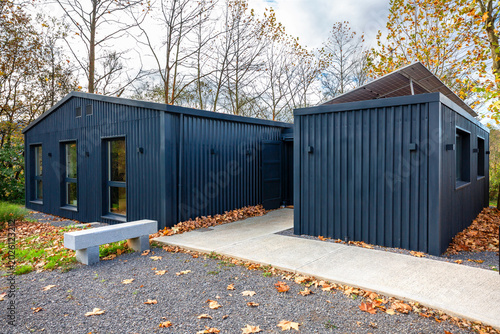 Modern modular house built with shipping containers features a dark corrugated exterior and solar panels, blending contemporary design with sustainable living in a natural autumn environment