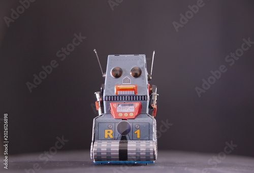 Classic vintage tin robot toy with orange and gray metallic finish on neutral . Retro collectible features antennas and tracked wheels. Nostalgic childhood toy representing 1950s science fiction era.
