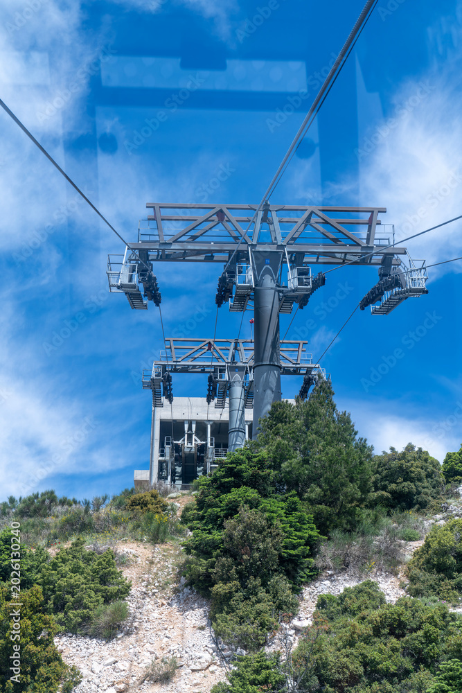 Obraz premium View from a cable car cabin approaching a massive metal support tower and station on top of a green mountain.