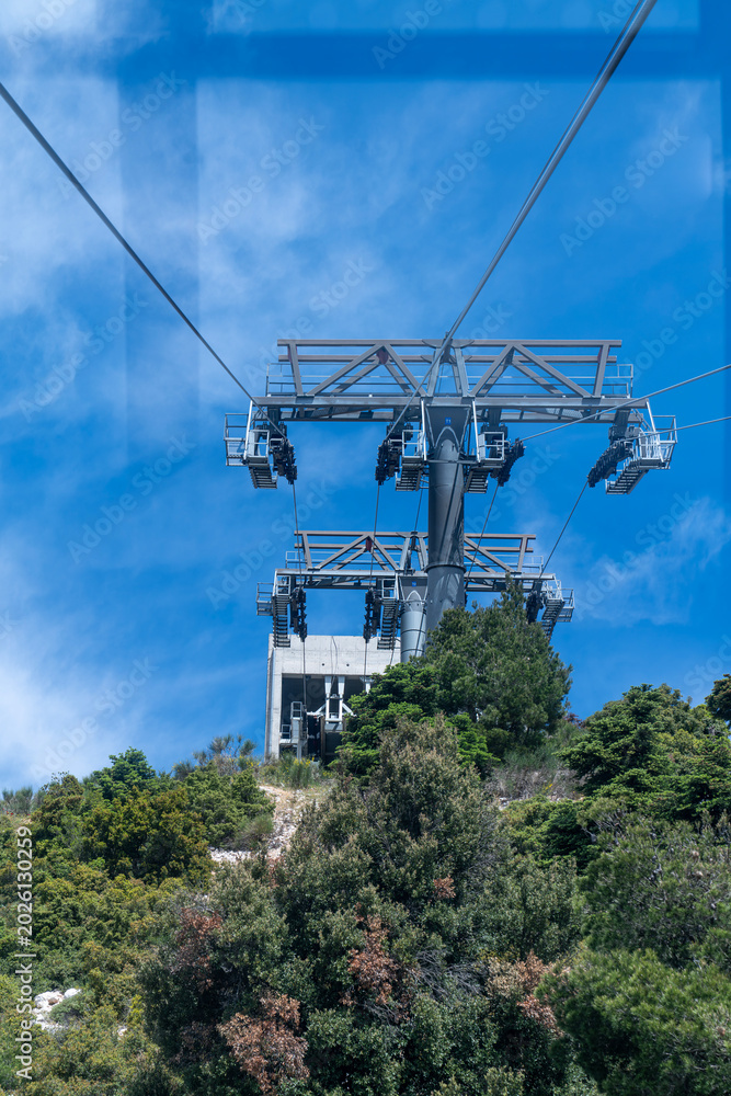 Obraz premium View from a cable car cabin approaching a massive metal support tower and station on top of a green mountain.