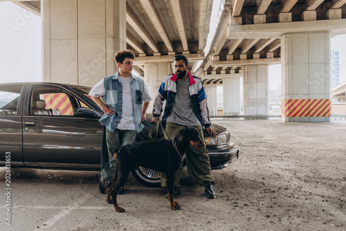 Two diverse male friends in streetwear fashion posing with a Doberman dog
