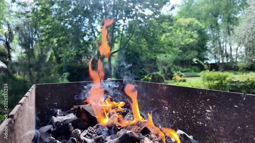 Slow motion closeup of burning charcoal and fire in metal mangal grill with smoke in sunny backyard garden outdoors