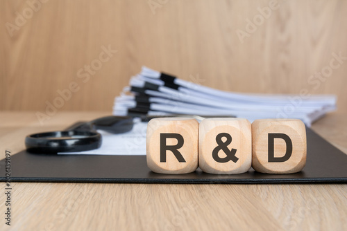 Wooden blocks with R D abbreviation on office desk with documents and magnifying glass research and development concept