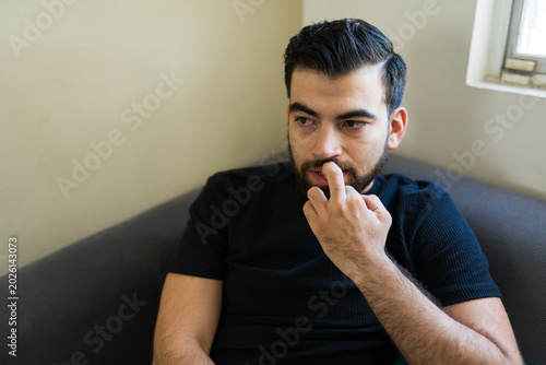 Photos Depressed man feeling worried or anxious, sitting alone at home confronting his
