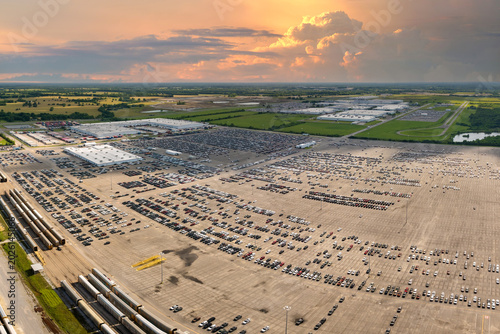 Industrial cargo trains at automotive factory loaded with new cars ready for transporting. Automaker parking lot with vehicles for sale