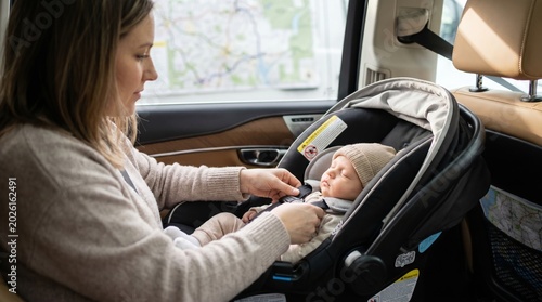 Mother secures sleeping infant in safety car seat. A family prepares for road trip with careful attention to safety. Ideal for parenting, travel, and child safety content.