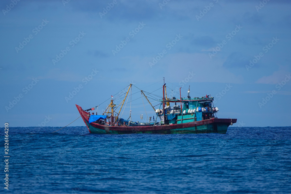 Obraz premium Traditional wooden fishing boat floating on calm tropical water near the Mentawai Islands. Working vessel sits alone against a soft blue horizon. Everyday marine life in remote parts of Indonesia.