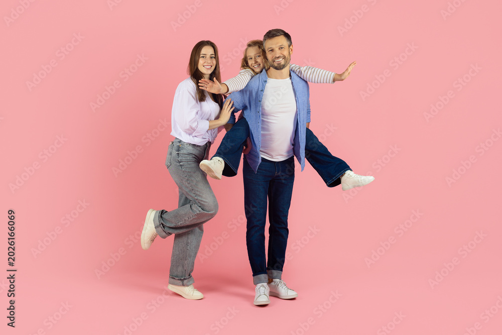 Obraz premium Cheerful caucasian family having fun together on pink studio background, posing playfully in a modern parenting and happy lifestyle concept portrait