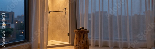 Shower corner with wooden stool and city view at dusk
