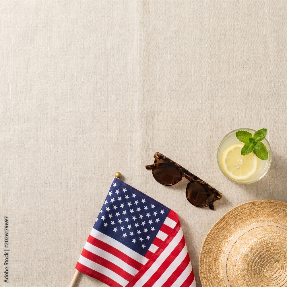 Obraz premium A refreshing summer picnic setup with a patriotic American flag, a straw hat, sunglasses, and a lemonade drink on a textured surface