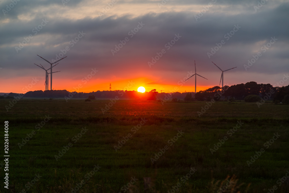 Obraz premium Dramatic sunrise over wind turbines in rural green landscape under dark storm clouds, conceptualizing sustainable energy and climate change transition 