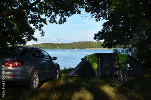Car and tent camping on a lake shore with a bicycle and speedboat. Active summer road trip