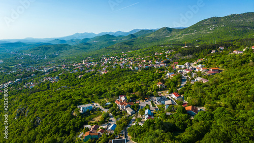 Fotografi Aerial view of a vibrant Hreljin village nestled among lush green hills and mountains in the Vinodol Valley, bathed in warm late afternoon sun