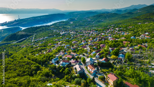 Foto Aerial view of a charming Croatian village nestled in lush hills overlooking the serene Kvarner Gulf and Bakar port in late afternoon light