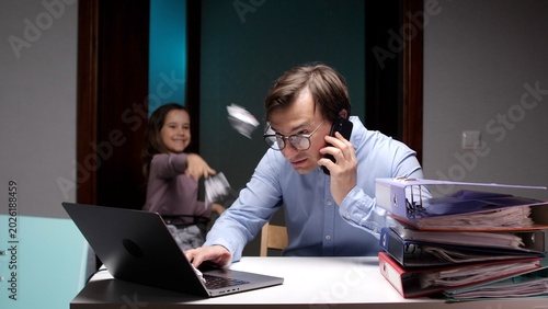 Obraz na plátně Overwhelmed father working from home on laptop and phone while a chaotic daughte