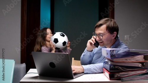 Fotografija Busy dad juggling a work call on his laptop while his daughter plays with a socc