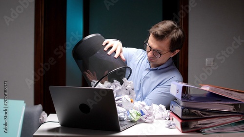 Photos Stressed businessman emptying a mesh trash can, scattering crumpled paper balls