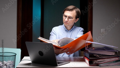 Bild auf Leinwand Business man wearing glasses checking financial documents in an orange binder at
