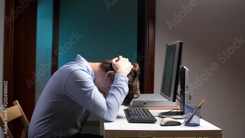 Foto Stressed office worker sitting at desk with head in hands, overwhelmed by work p