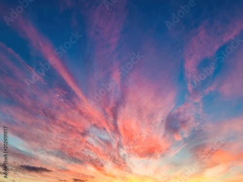 A vibrant sunset sky with hues of pink, orange, purple and blue clouds radiating out from the horizon