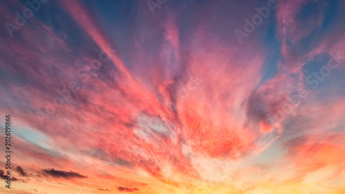 A vibrant sunset sky with hues of pink, orange, purple and blue clouds radiating out from the horizon