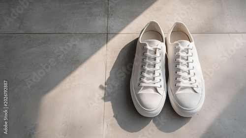 Pair of clean white canvas sneakers on concrete floor with dramatic diagonal sunlight and shadows