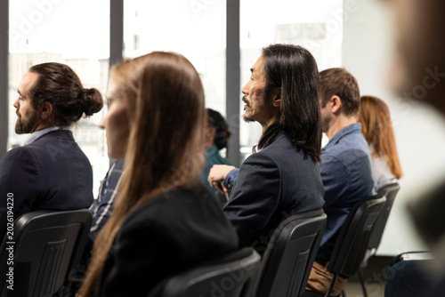Fotografía Asian businessman listening to presentation with diverse audience group, business conference meeting with speaker