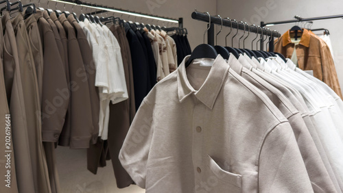 Minimalist fashion boutique interior with neutral clothing collection on racks, elegant beige shirts trousers jackets in modern retail showroom, contemporary apparel shopping concept
